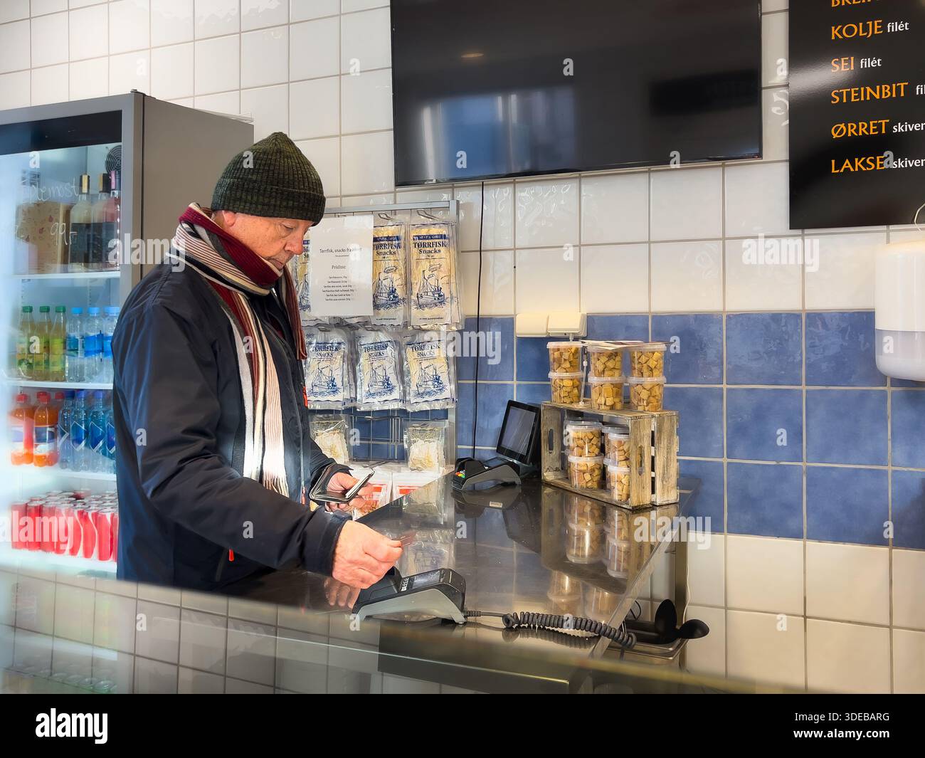 Slow everyday independent aging senior lifestyle with an older man paying at a shop counter indoors, cashless payment and calm routine reflecting mode Stock Photo