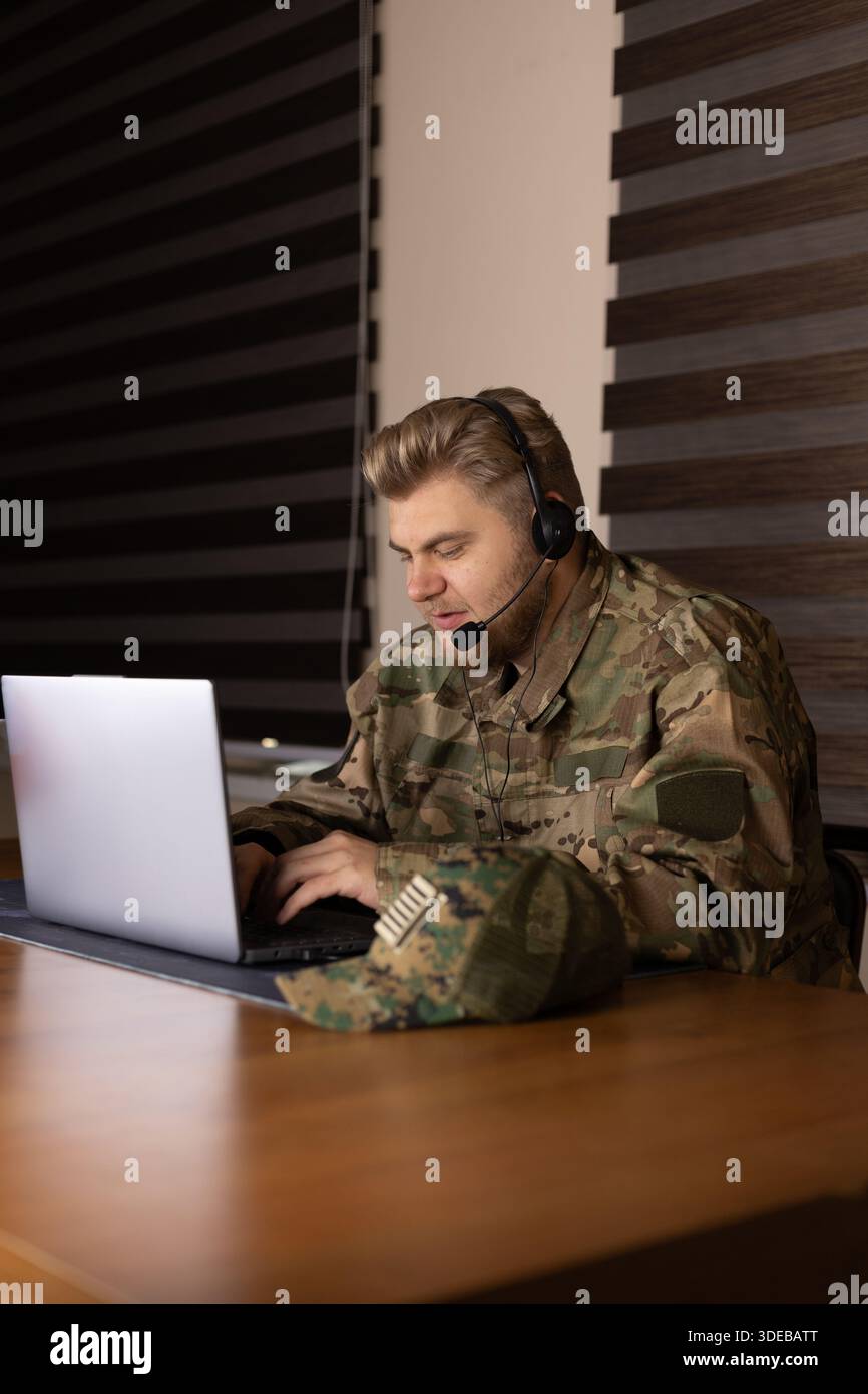 Military man in uniform working with a laptop in dark room. Stock Photo
