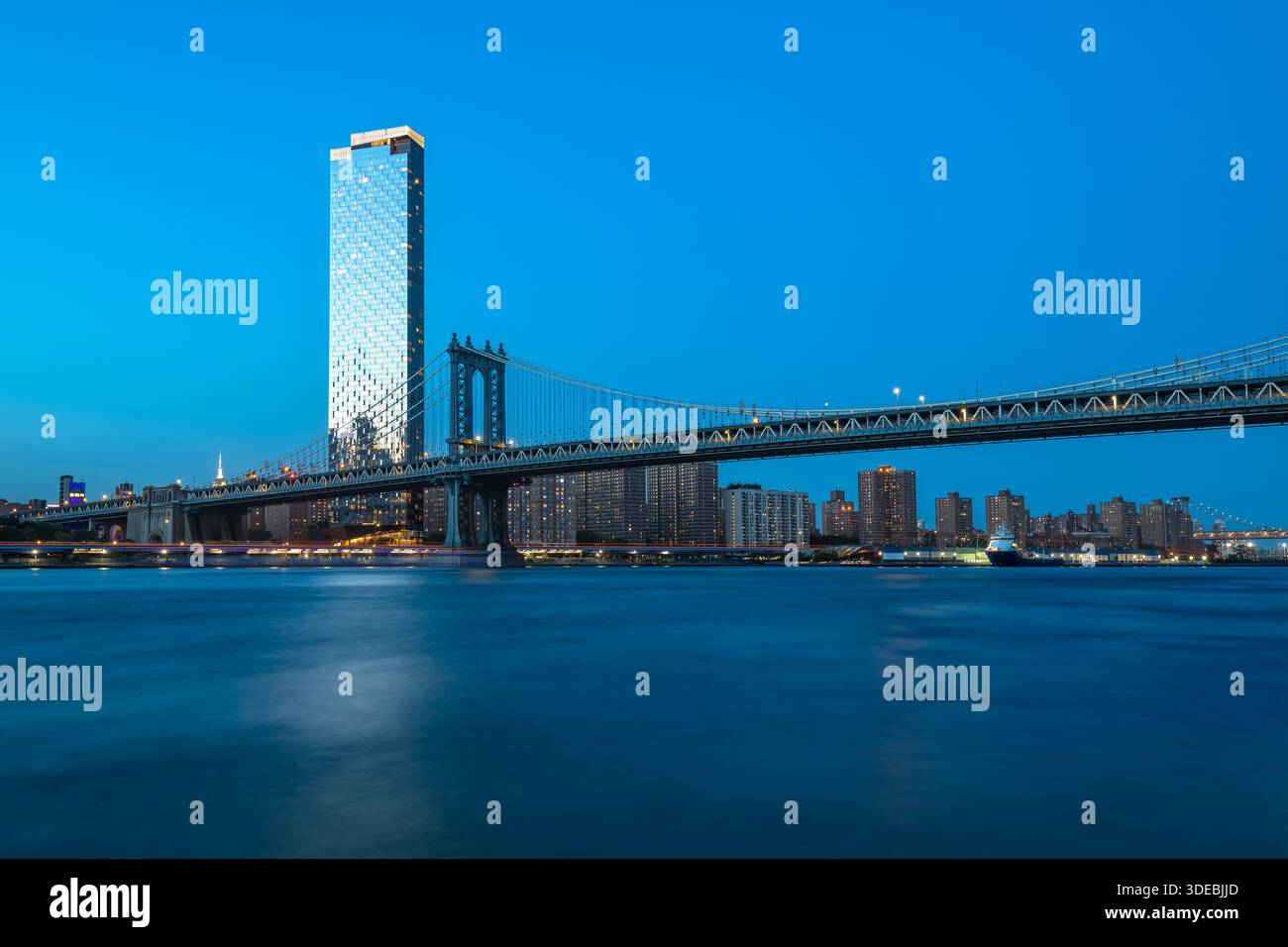 The iconic Manhattan Bridge spans the East River during the serene blue hour, connecting Brooklyn and Lower Manhattan. Stock Photo