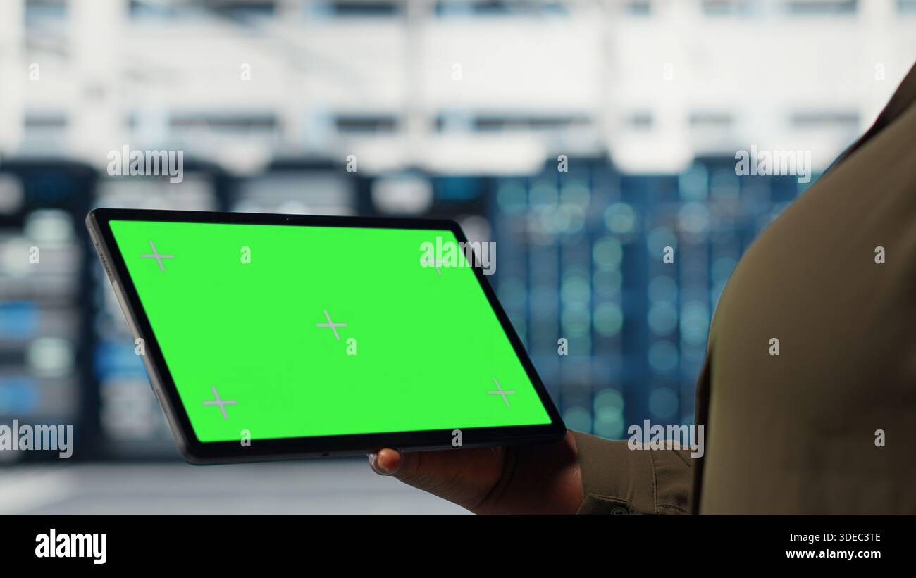 Server room admin uses isolated screen tablet to increase supercomputers workload capacity. Data center worker configures gear with chroma key device notebook, improving processing speed, camera B Stock Photo