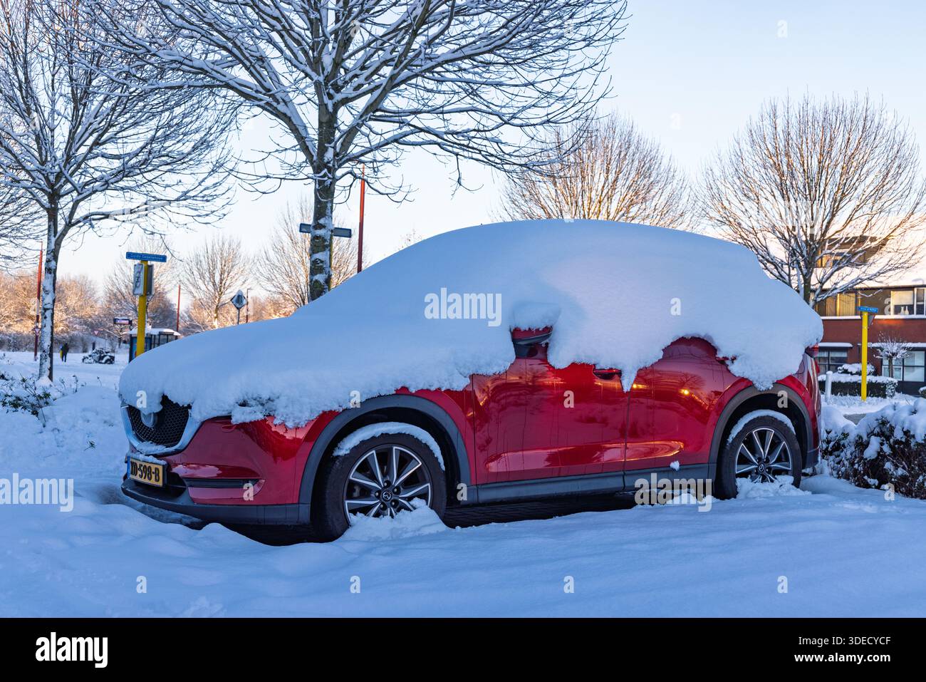 Red SUV car parked in a residential street completely covered with a thick layer of white snow during a freezing cold winter day in the Netherlands. U Stock Photo