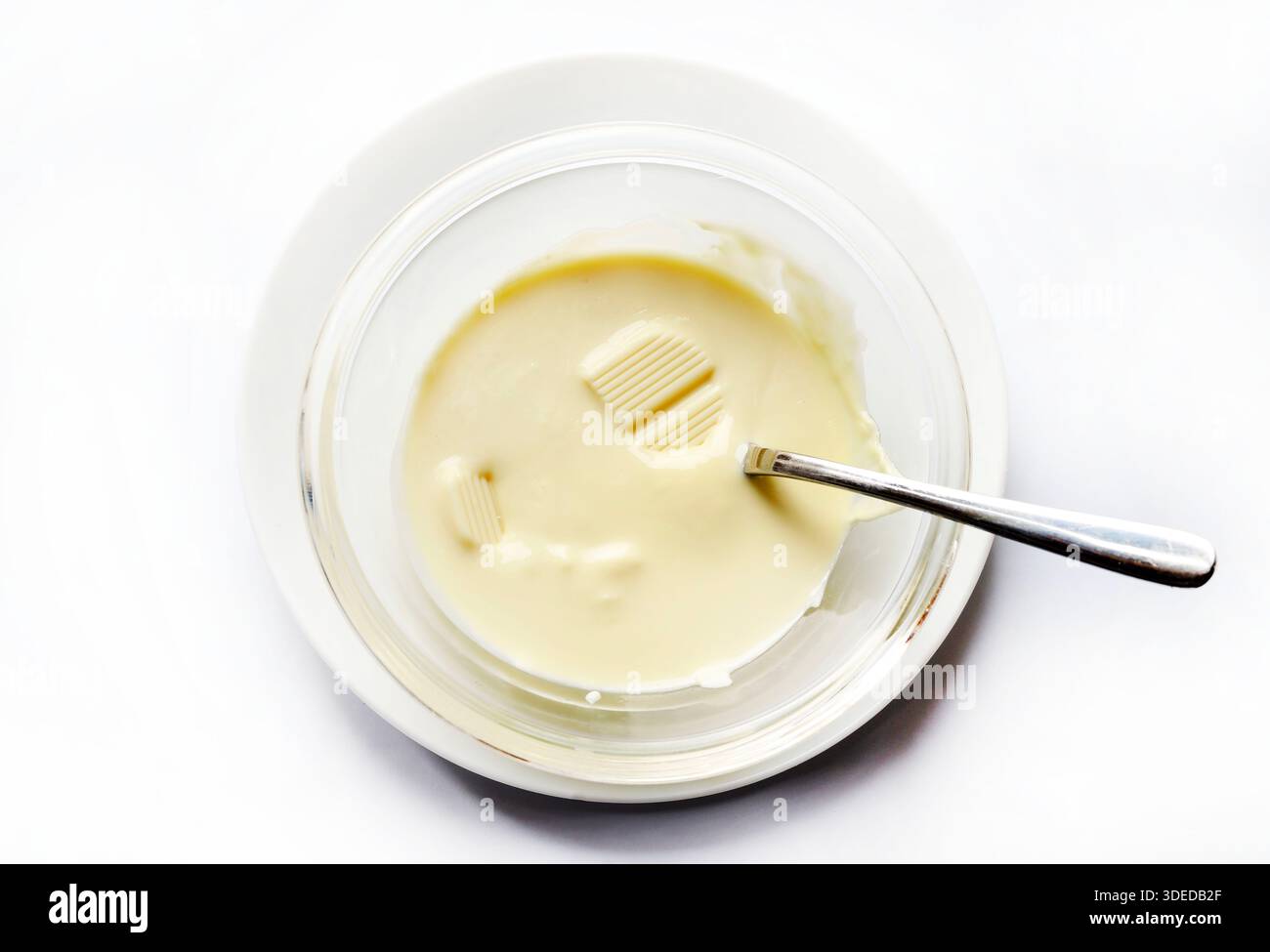 Melted white chocolate in a glass bowl isolated on a white background. Overhead view. Stock Photo