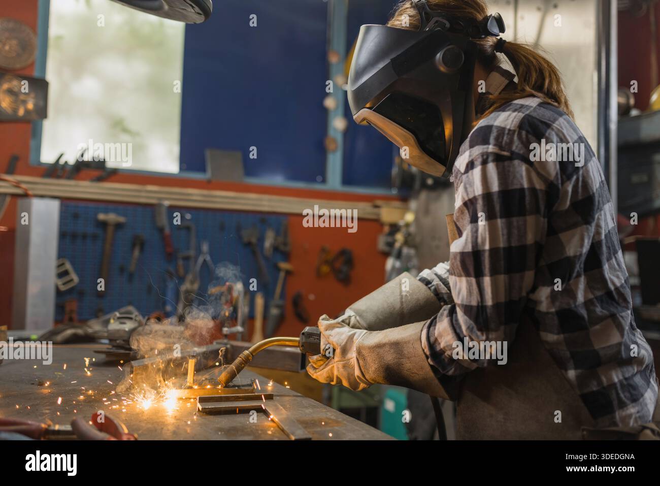 A female welder is working in a workshop, showcasing her skills in a technical role. This highlights womens contributions in industry. Stock Photo