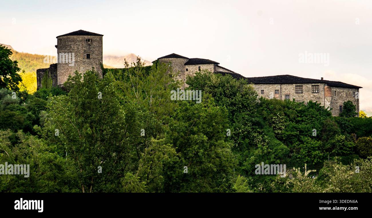 Historic stone castle surrounded by lush green trees and hills. Stock Photo