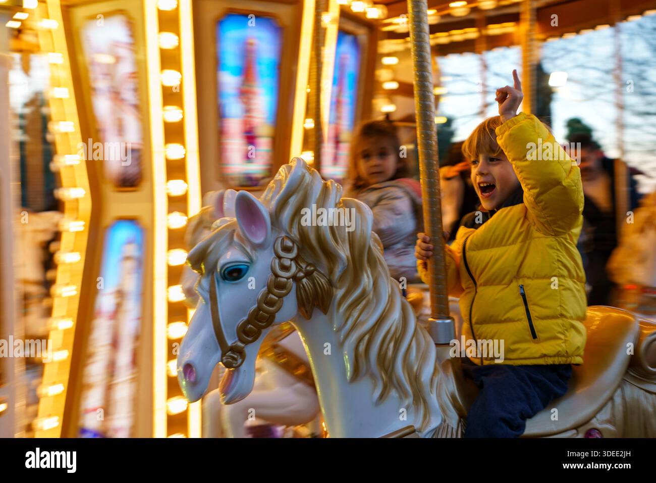 Excited children riding a brightly lit carousel with decorative horses during the evening at a festive fair Stock Photo