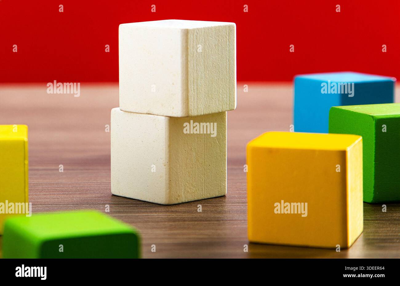 Wooden toy blocks creating a structure on a wooden table with a red background Stock Photo