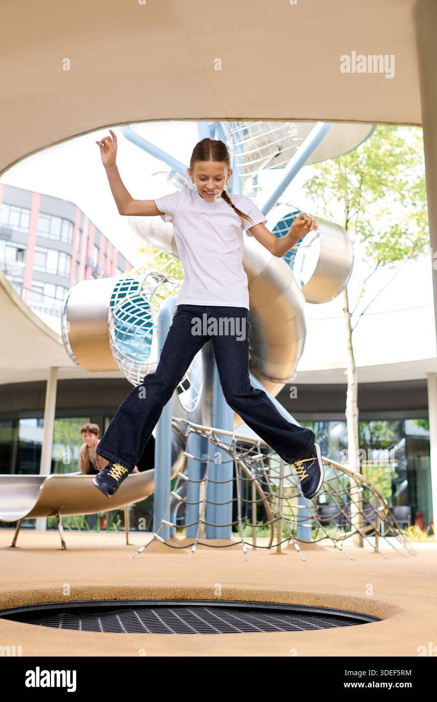 A child plays joyfully, jumping high with glee in a vibrant playground, surrounded by autumn colors. Stock Photo