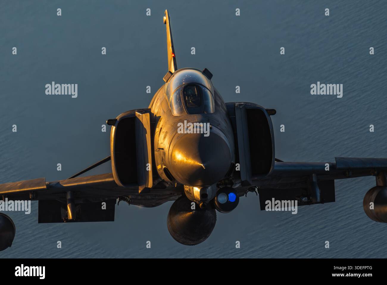 This air-to-air photograph depicts a Hellenic Air Force McDonnell Douglas F-4E Phantom II in close-up view during Athens Flying Week 2025. The aircraft is a twin-engine, supersonic fighter powered by two General Electric J79-GE-17A afterburning turbojet engines. Key features include the cockpit, pilot, canopy, fuselage, wings, tail assembly, vertical stabilizers, air intakes, and aerodynamic surfaces, demonstrating precision, maneuverability, and operational capability. Stock Photo