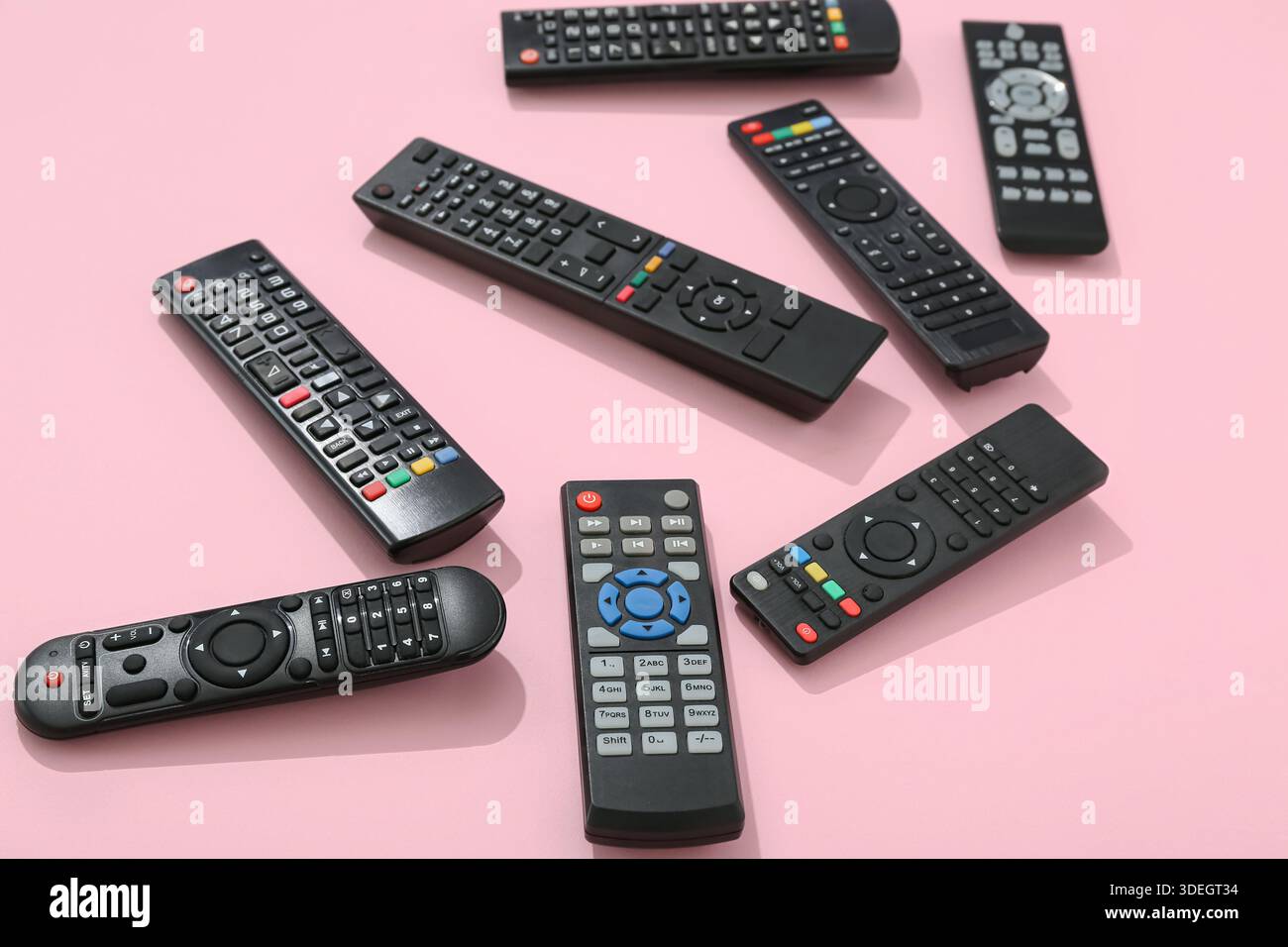 Different modern TV remote controls on pink background Stock Photo
