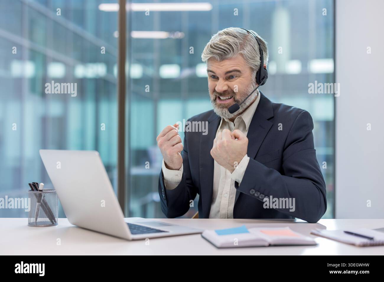 Male professional customer support agent sitting at a desk with a laptop, looking frustrated and angry, experiencing stress and problems during an intense online communication Stock Photo