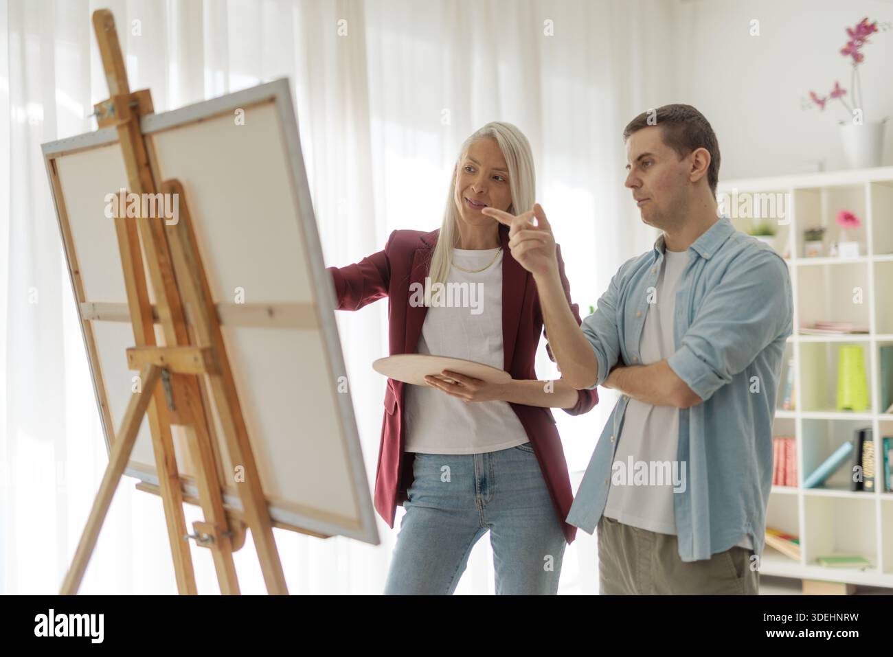 Focused artists discussing a canvas on an easel inside an art studio Stock Photo