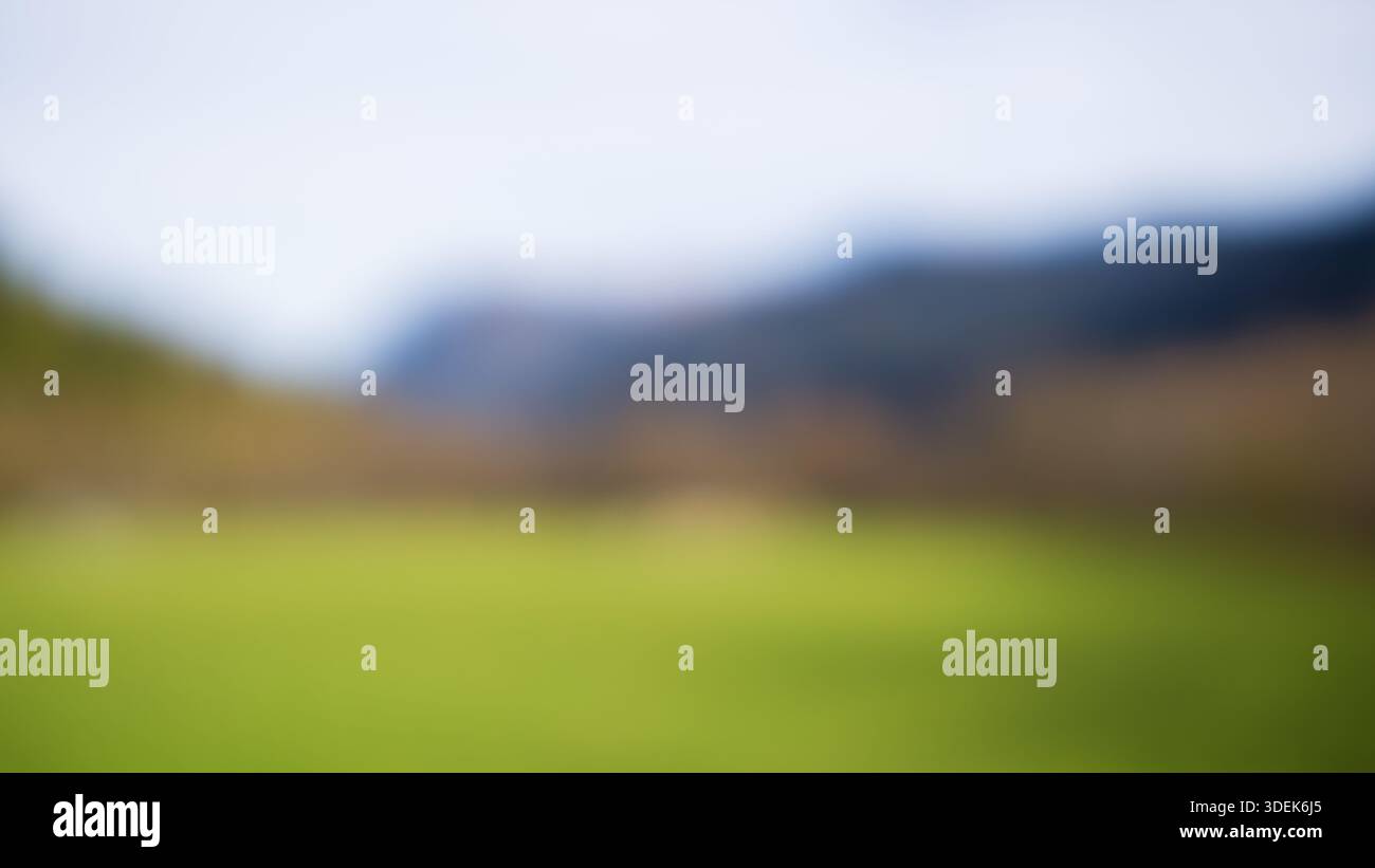 Soft focus creates smooth color transitions between grass, hills, and distant mountains. Stock Photo