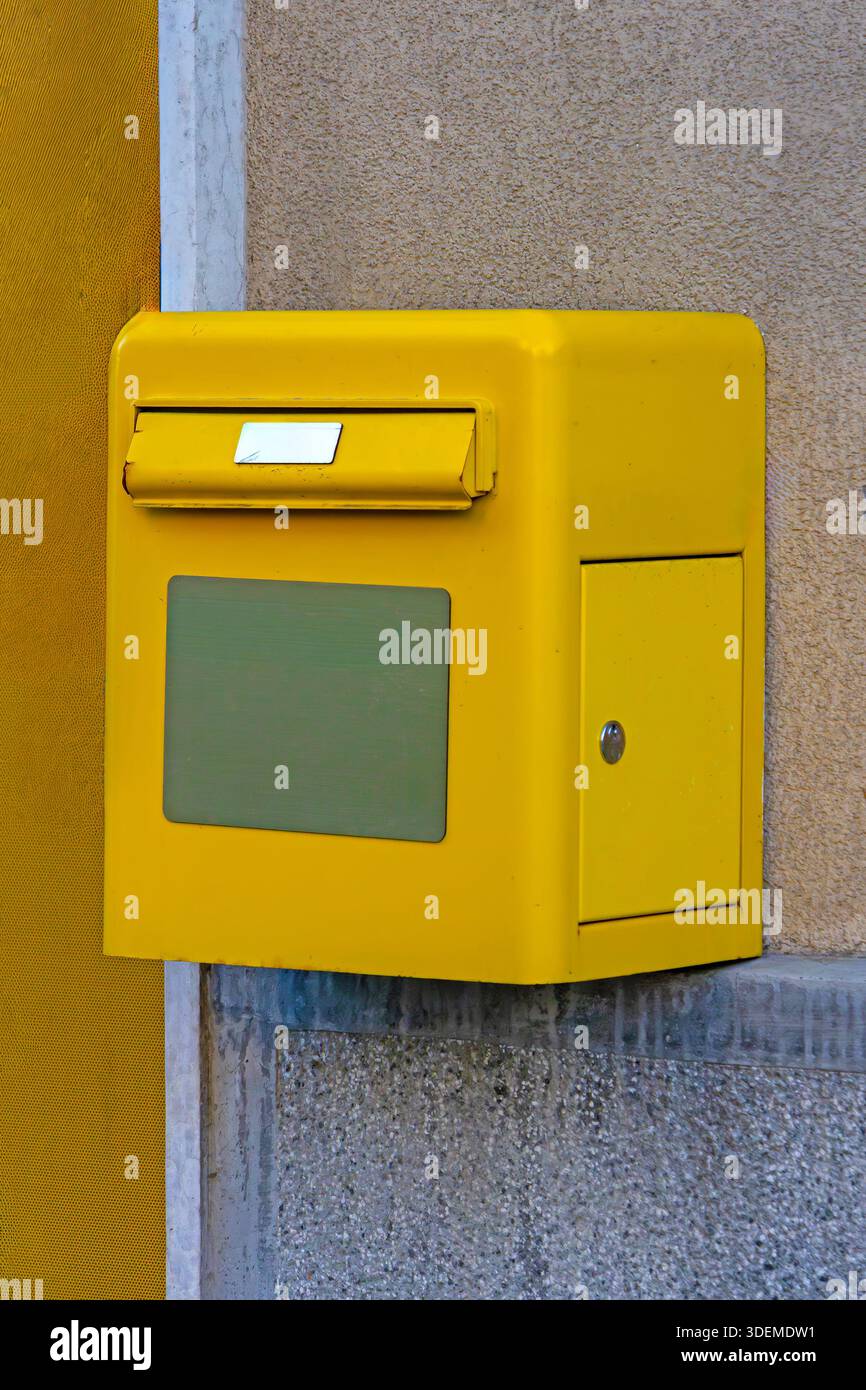 Yellow post office box hanging on building wall facade outside Stock Photo