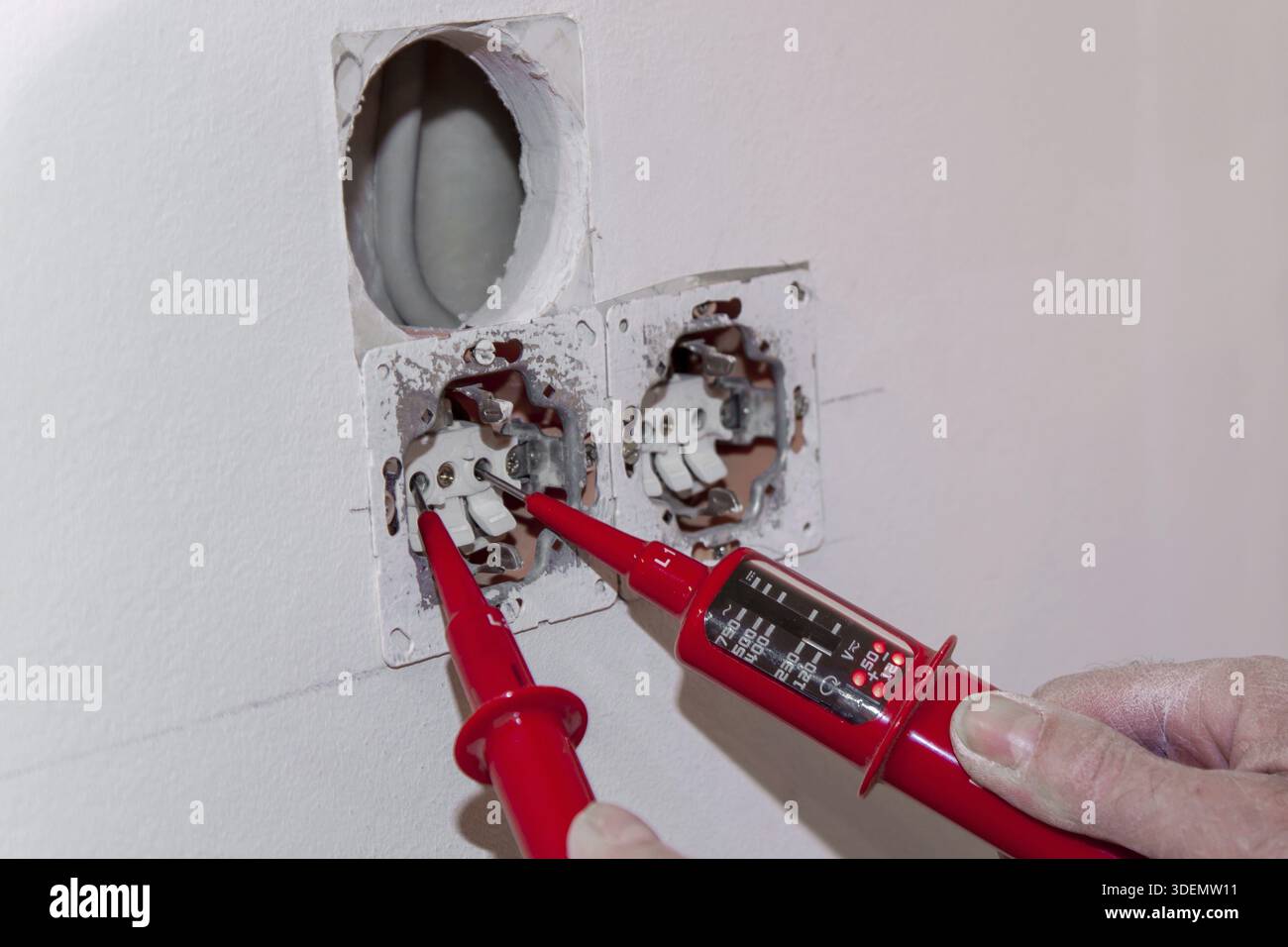 Hand of Electrician testing for electricity with a voltage tester. Electrician checking wall socket with voltage tester. Touchless Voltage tester hand Stock Photo