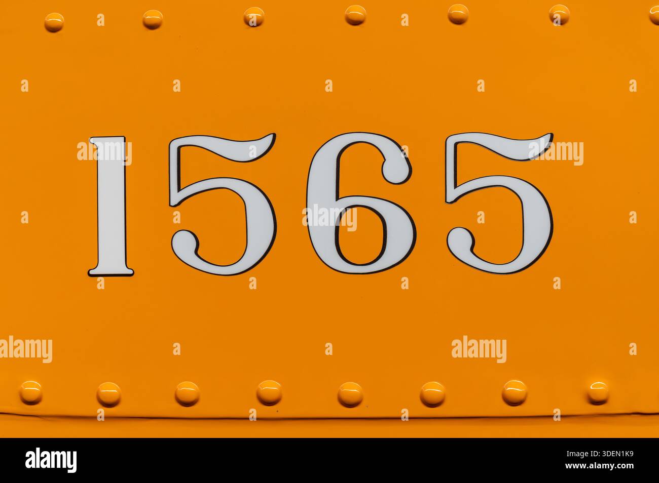 White numerals 1565 painted on an orange metal surface with visible rivets Stock Photo