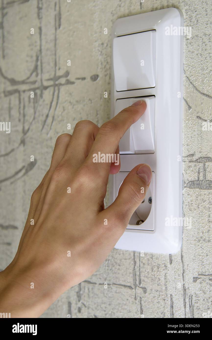 Female hand on white light switch key Stock Photo