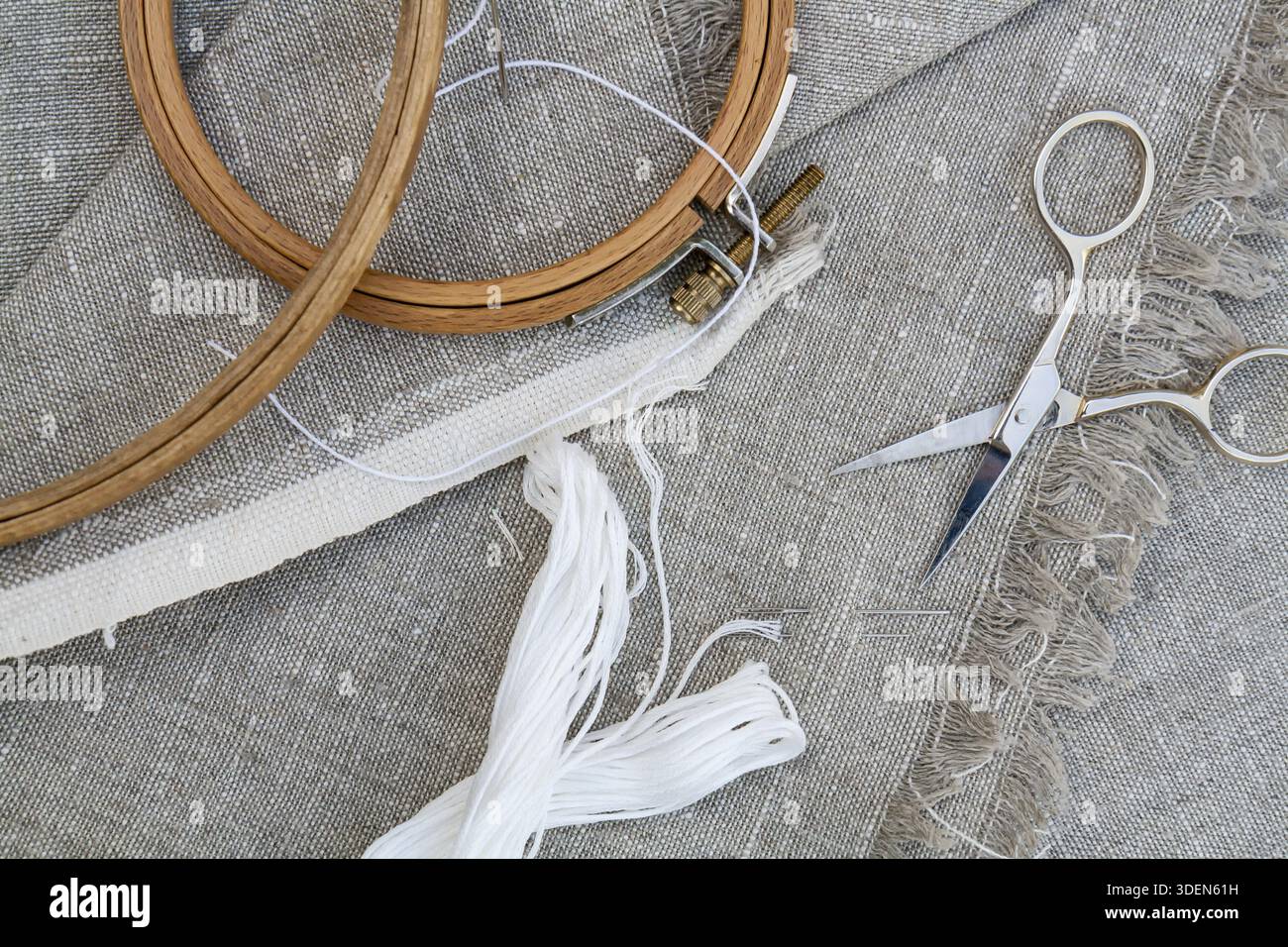 Set for embroidery, garment needle, thread, scissors and embroidery hoop on unbleached linen fabric. Top view Stock Photo