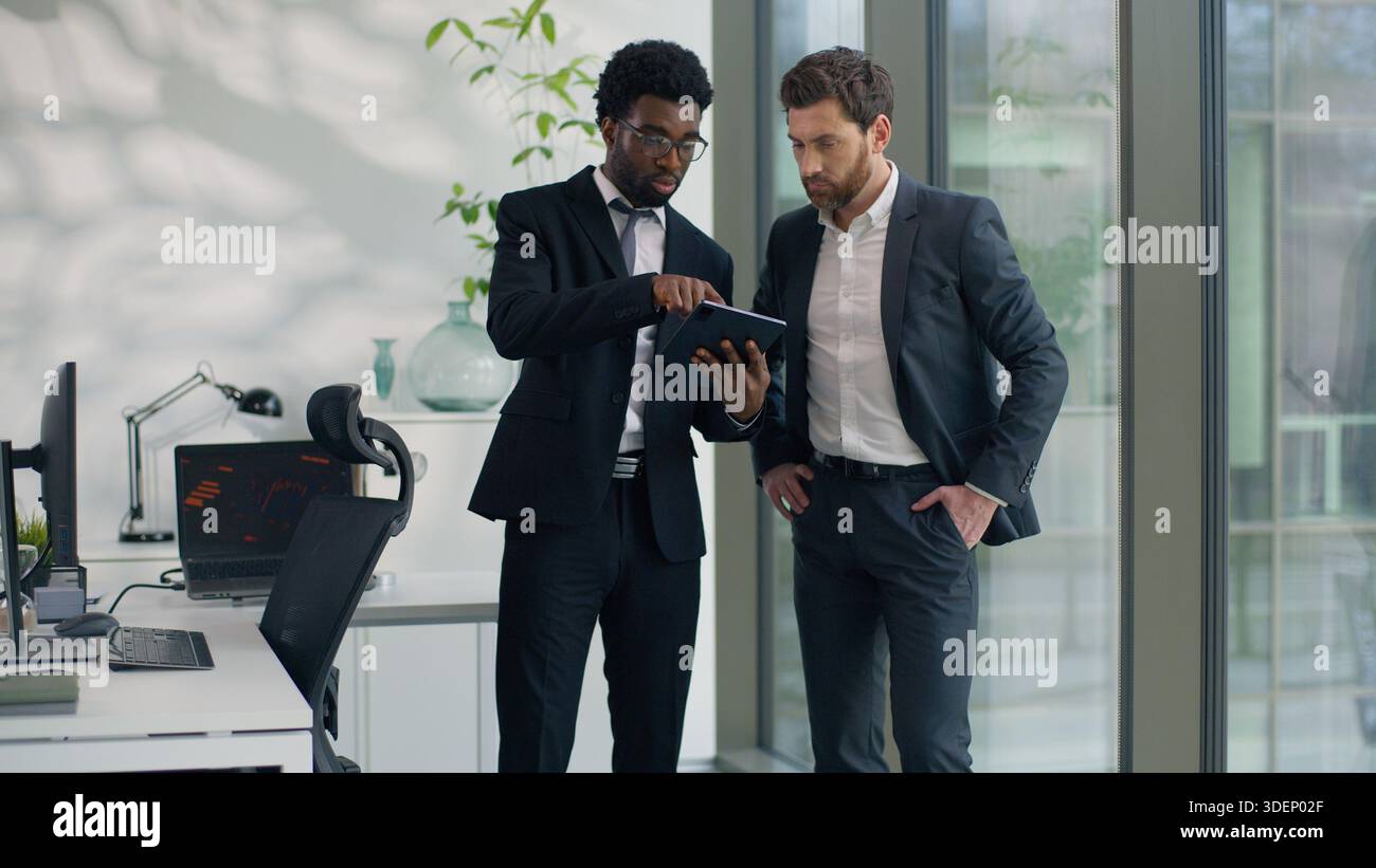 Two diversity businessmen talking in office using modern digital tablet together talk multiethnic business men male co-workers discussing online Stock Photo