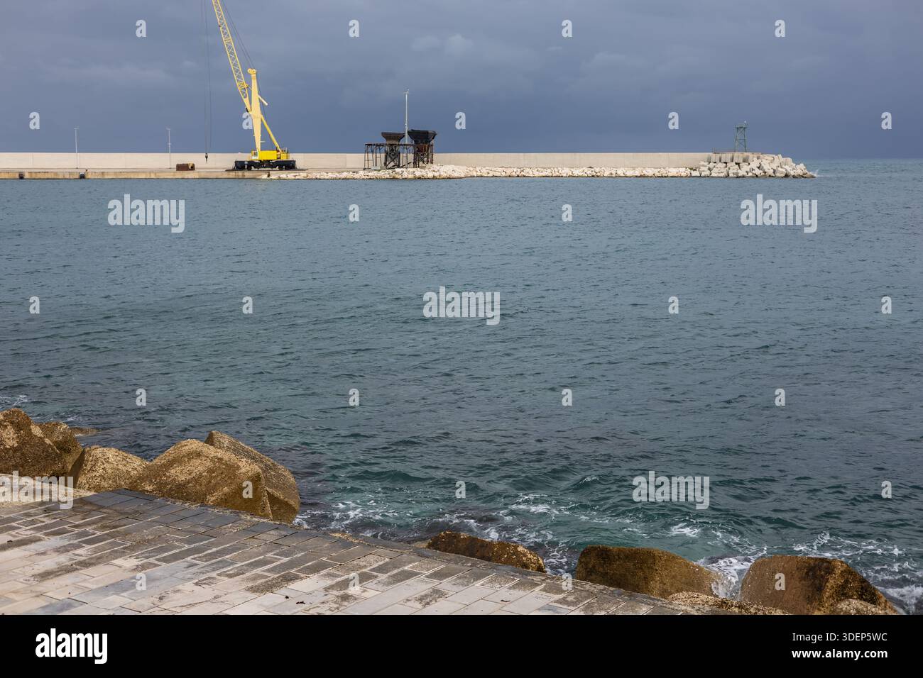 industrial yellow crane on a concrete pier under a stormy dark sky ...