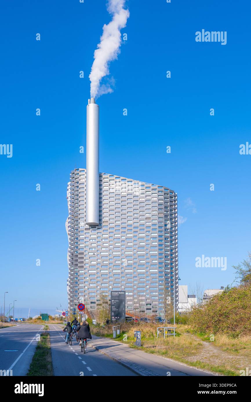 Visitors admire the innovative architecture of Amager Bakke, a waste-to-energy plant in Copenhagen. Its distinctive look and recreational features invite exploration in the clear blue sky. Stock Photo