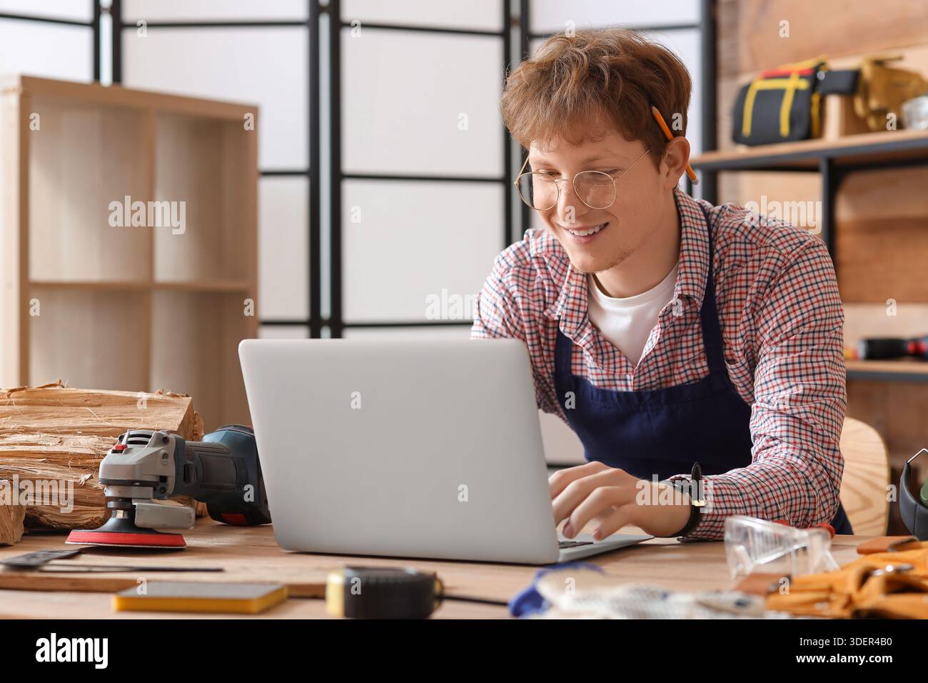 Young carpenter using laptop at table in workshop Stock Photo