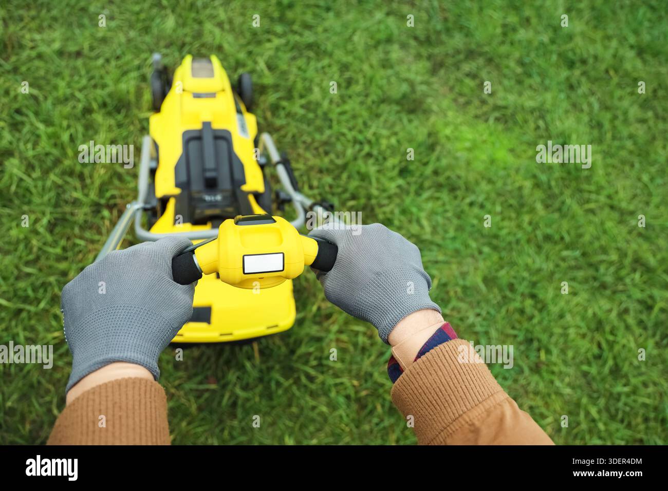 Male hands using modern lawn mower outdoors, top view Stock Photo