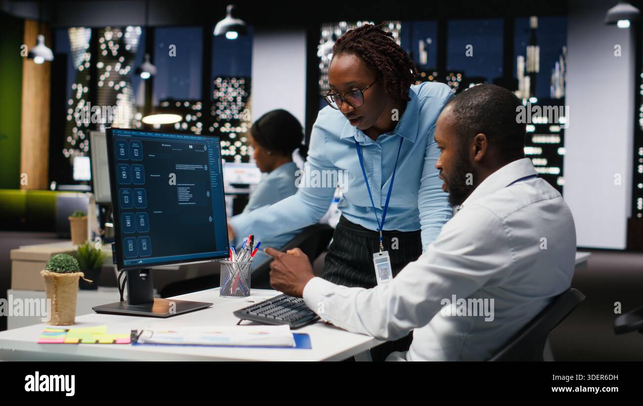 Black IT engineers team developing app and software algorithm on pc, working in the office late at night. Specialists use digital tools and focuses on script engineering and coding. Stock Photo