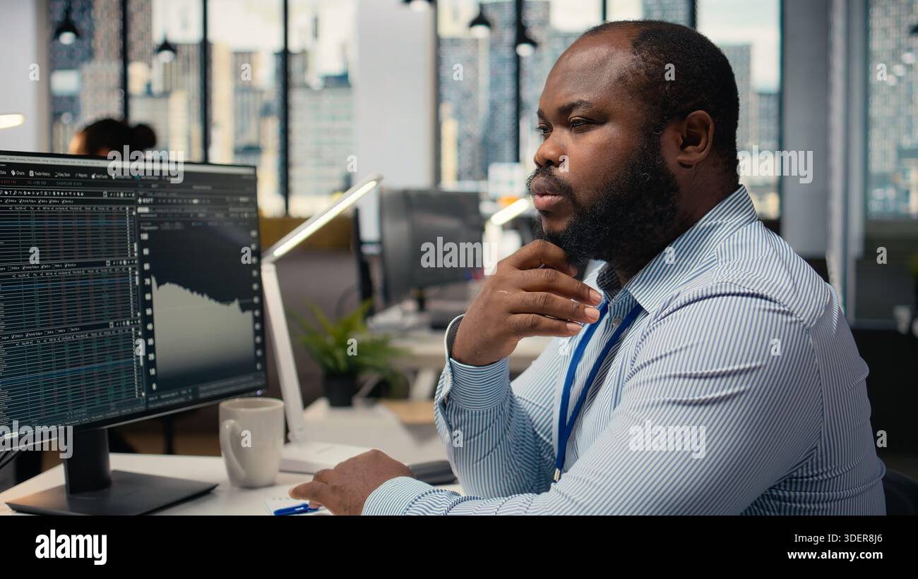Close up of trader analyzing stock exchange analytics, doing thinking, evaluating trading strategy in prop firm office. African american man brainstorming, assesses risk in financial markets Stock Photo