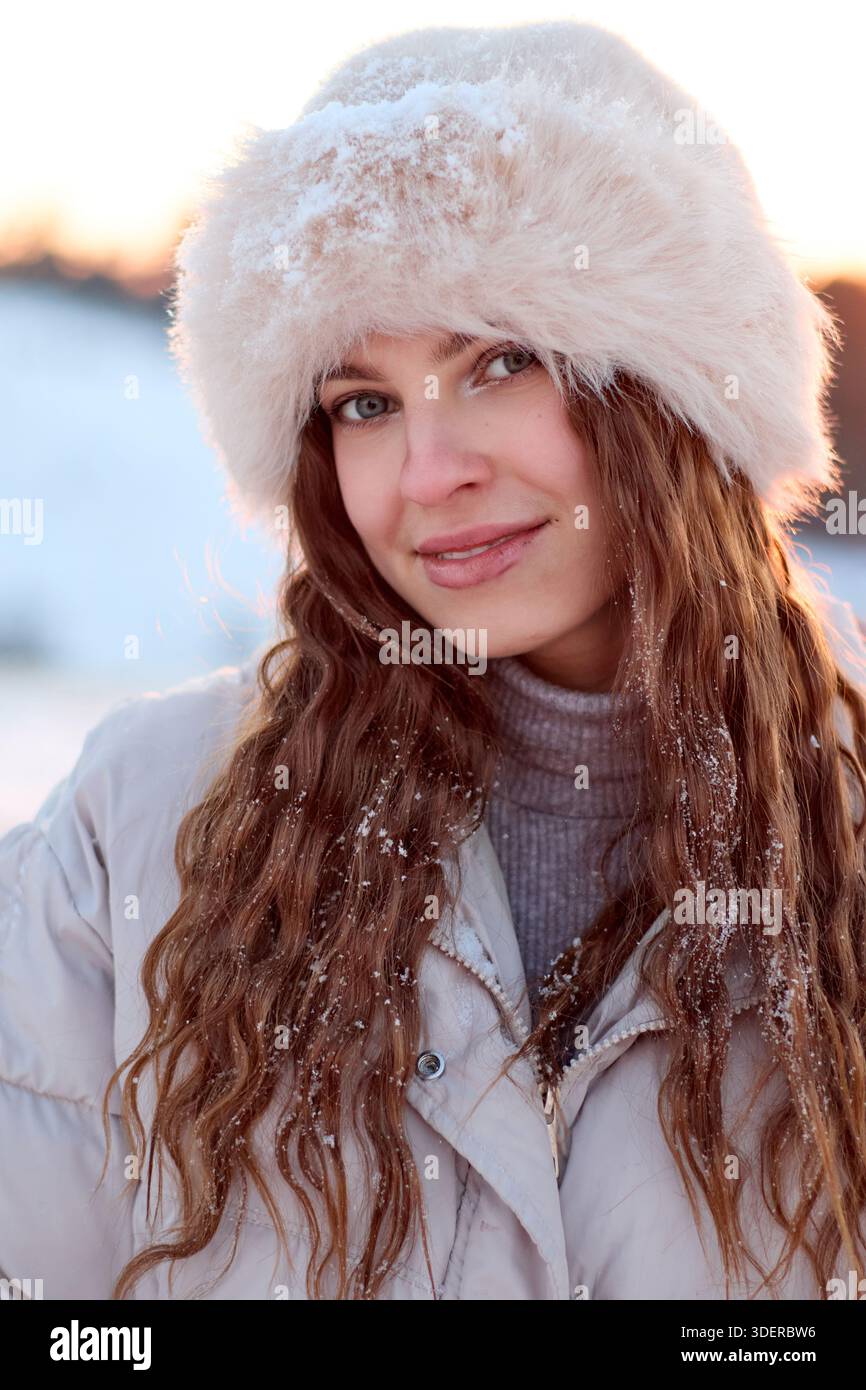 This image captures the serene beauty of a young woman in a winter landscape. The subject, a beautiful woman with long, curly brown hair, is the focal Stock Photo
