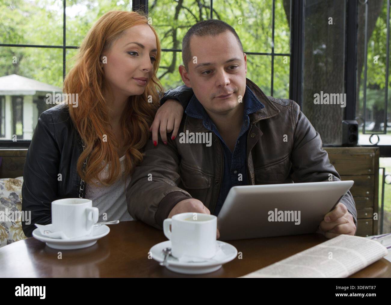 Two students drinking coffee and having fun with tablet In cafeteria Stock Photo
