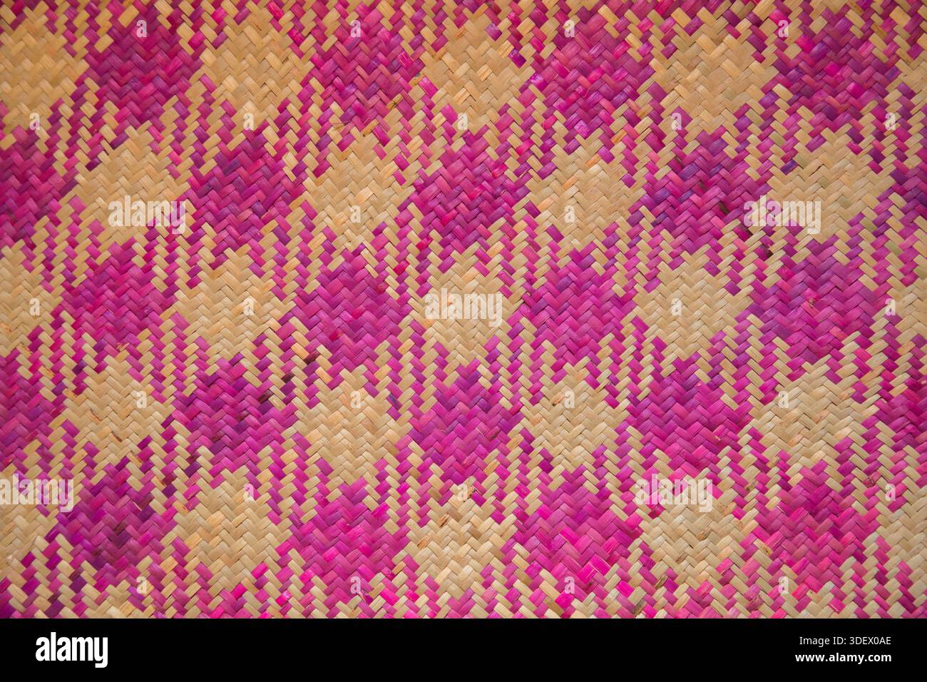 Woven mat in magenta and plain beige-coloured raffia. Used on the floor of a local home. Antsaharoa, village on the outskirts of Fianarantsoa.  Woven mats are a fundamental element of Malagasy life and culture, highly valued in traditional homes in villages like Antsaharoa, near Fianarantsoa. The use of vibrant magenta and plain beige-coloured raffia highlights the artisanal skills of the Betsileo people. Stock Photo