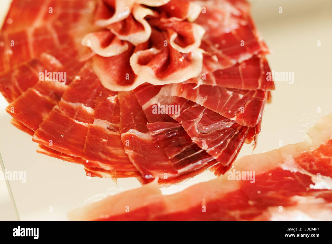 Close-up of thinly sliced cured ham arranged in overlapping layers, showing texture and rich color. Stock Photo