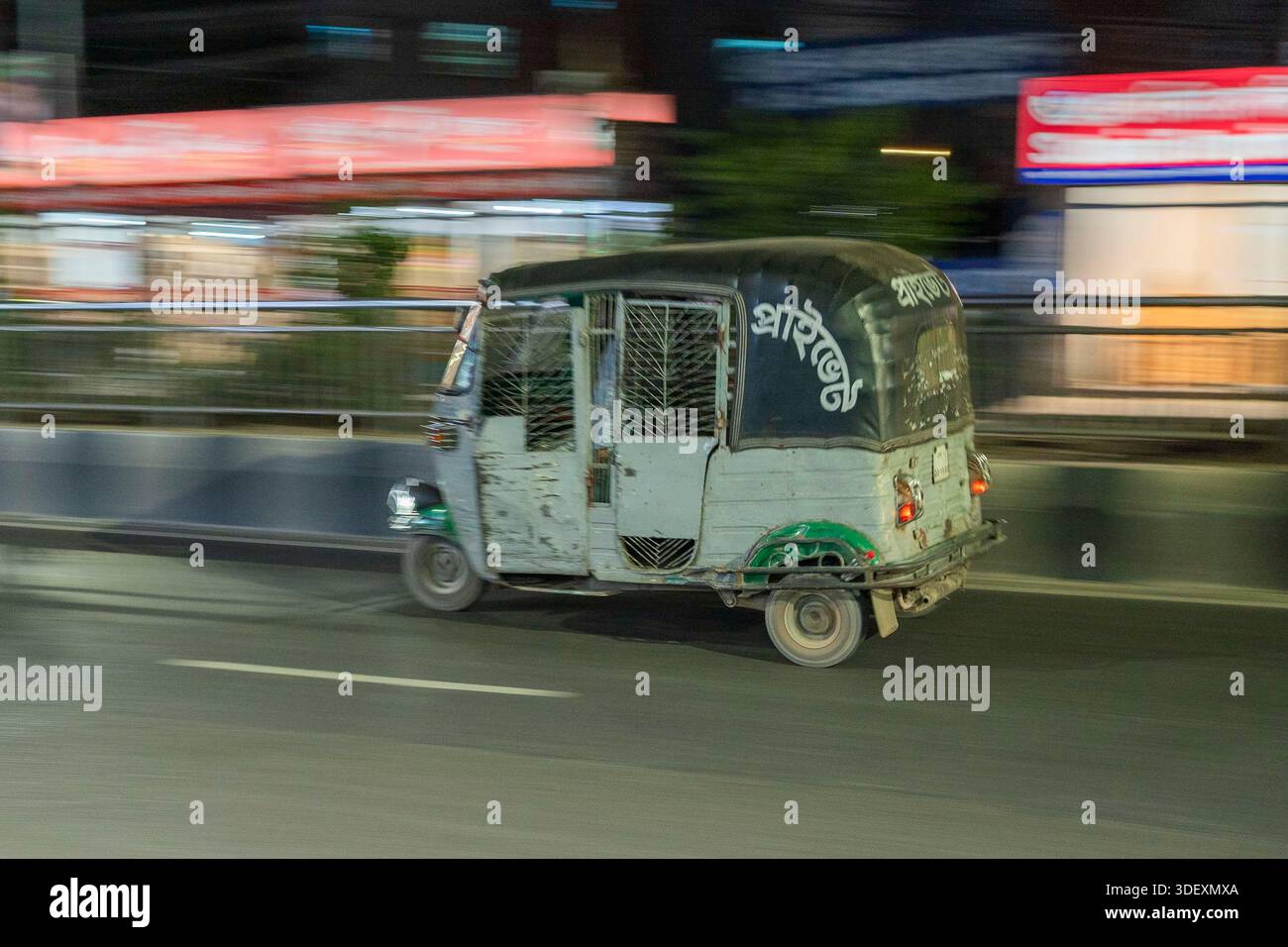 A green auto-rickshaw speeds through Dhaka at night. Motion blur ...