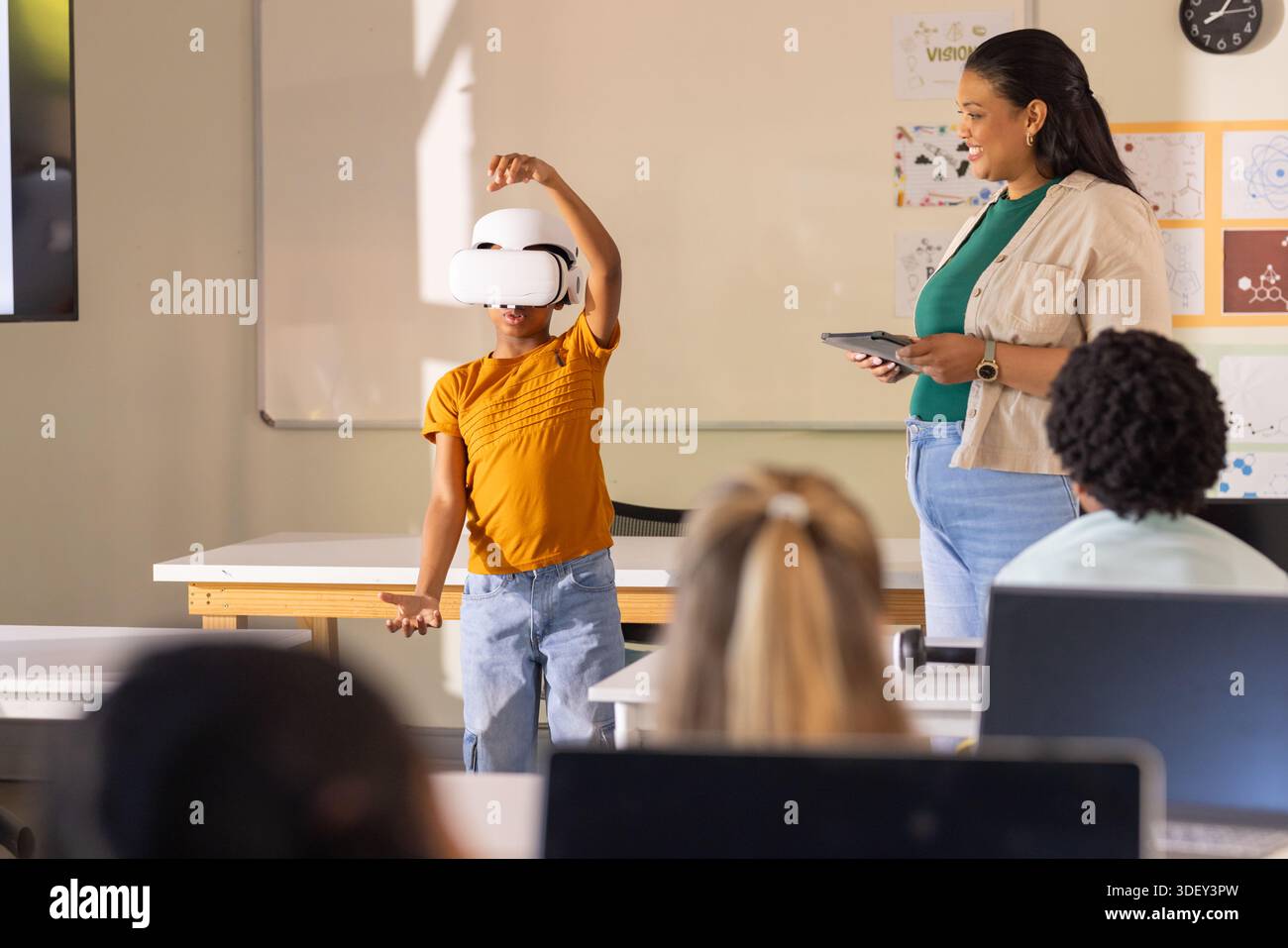 Teacher with students in classroom watching youth presenting VR headset with teacher holding tablet Stock Photo