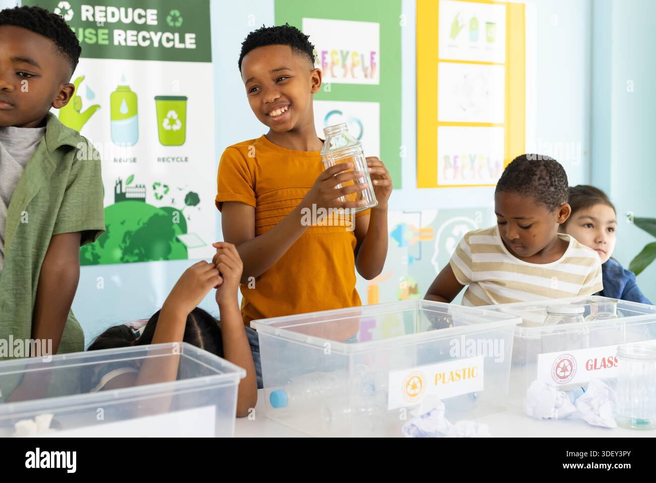Diverse children gathering at school table holding glass jar and sorting PLASTIC and GLASS bins Stock Photo