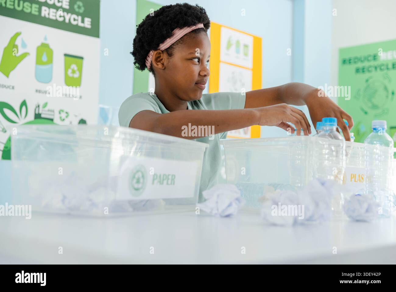African American youth wearing green tee and pink headband sorting bottles into labeled class bins Stock Photo
