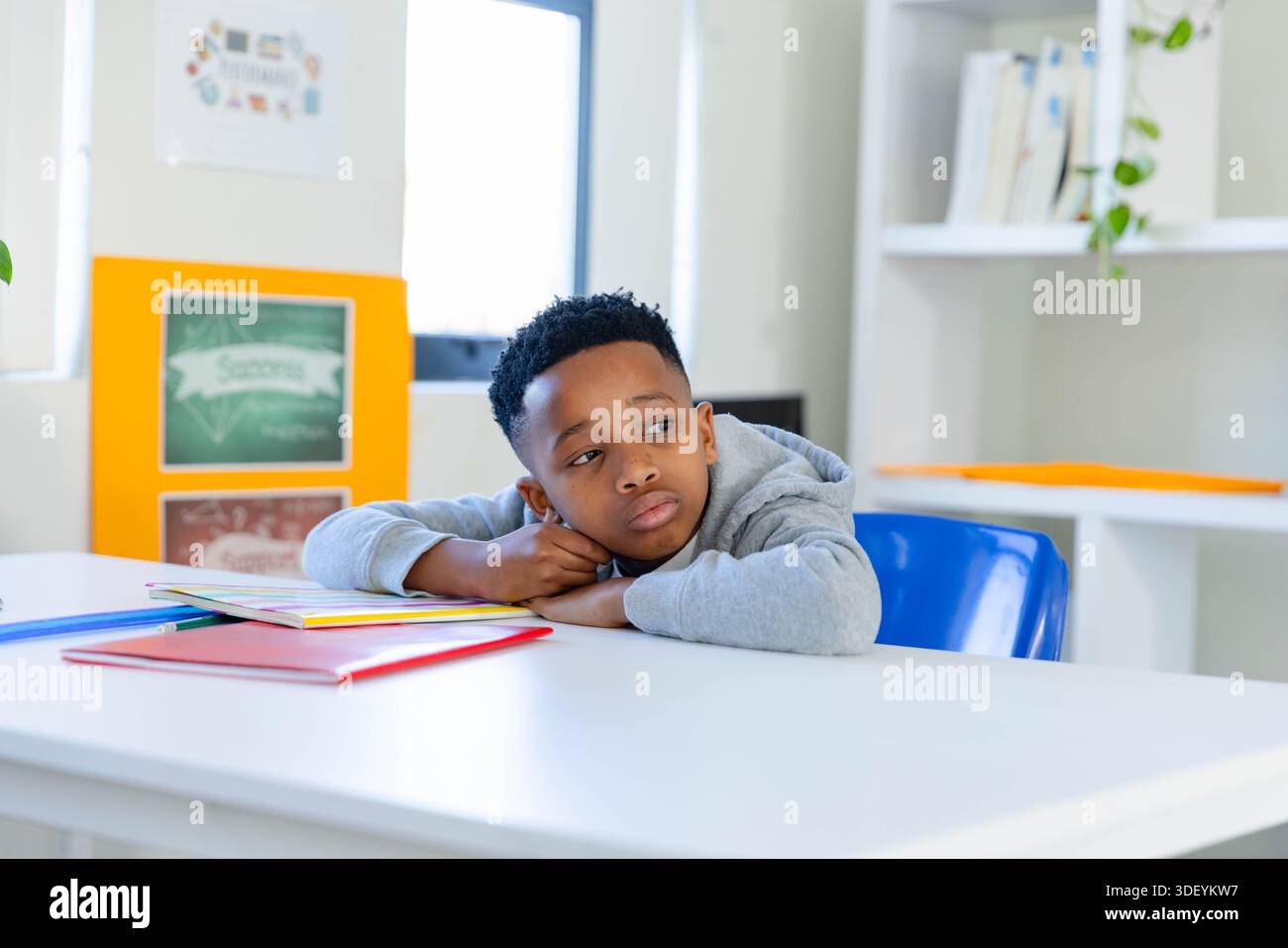 Adolescent African American male student sitting on blue chair at class table with colorful folders Stock Photo