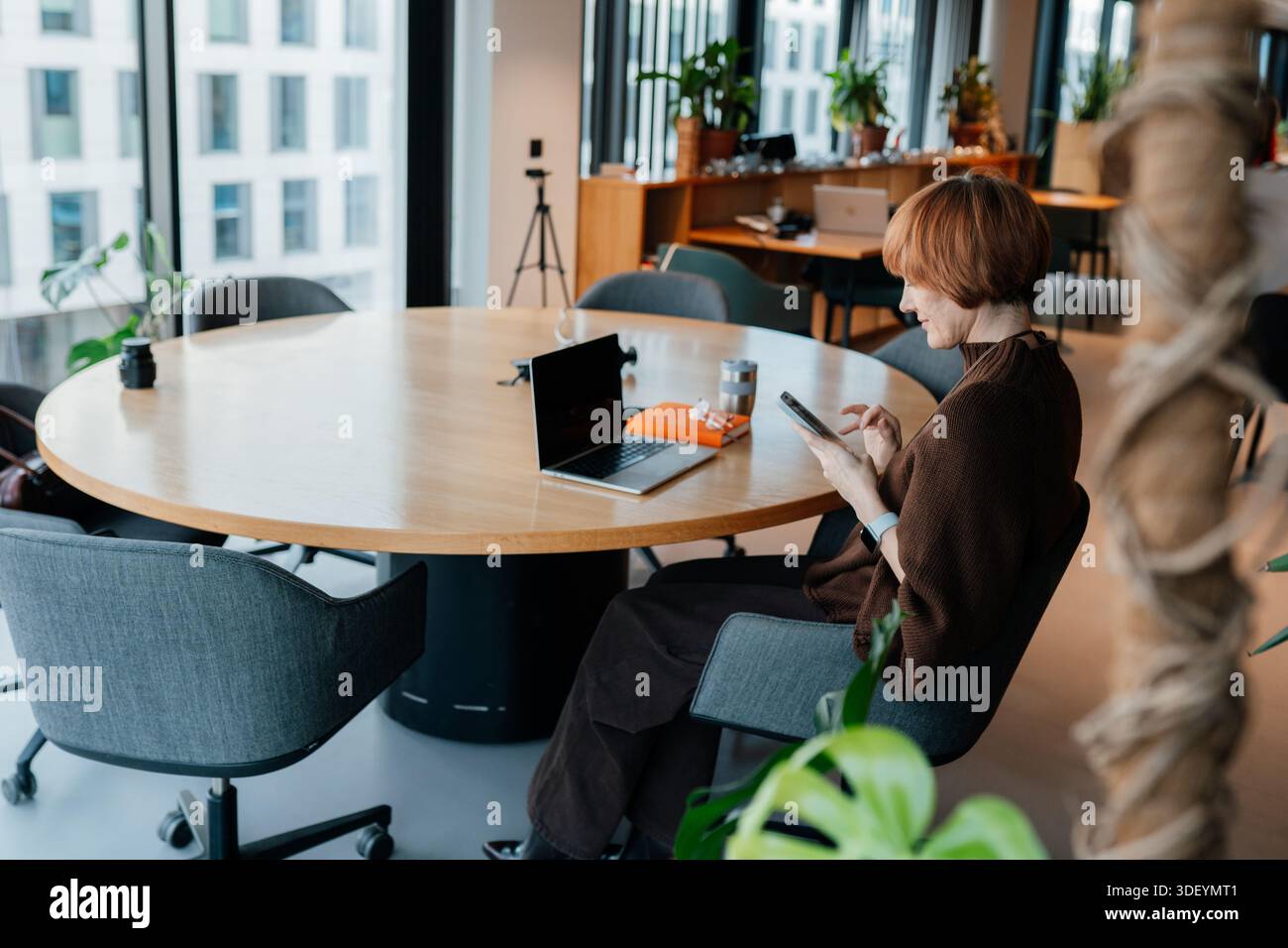 Middle age female using smartphone during quiet work moment indoors Stock Photo