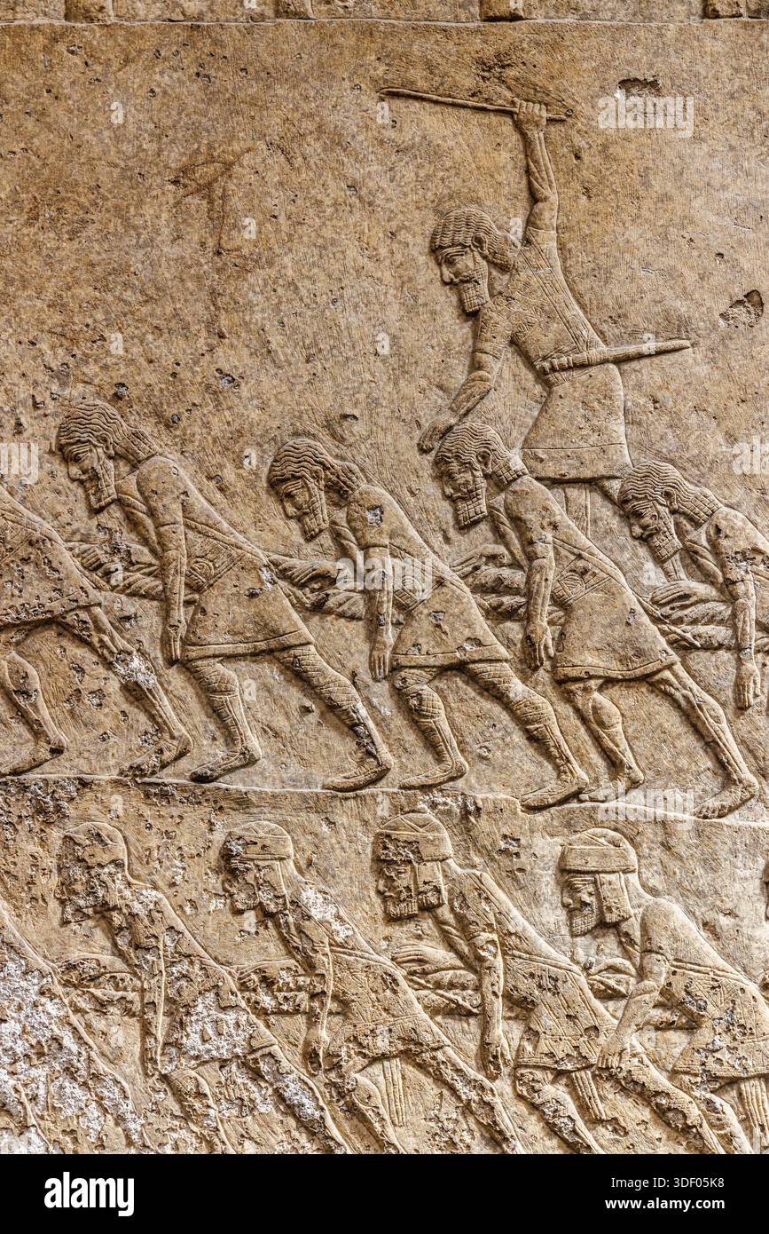 Assyrian wall design, captive men pulling a sledge with an overseer whipping them on, British Museum, London, England, UK Stock Photo