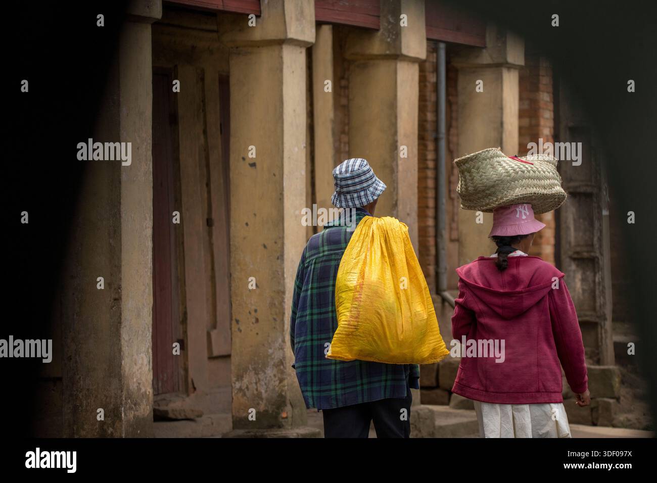 Malagasy couple in western clothing and hats carrying produce and walking away from the camera, Central Highlands, Behenjy, Madagascar.  In Madagascar, carrying loads on the head is a centuries-old traditional practice that remains a defining visual of daily life Stock Photo