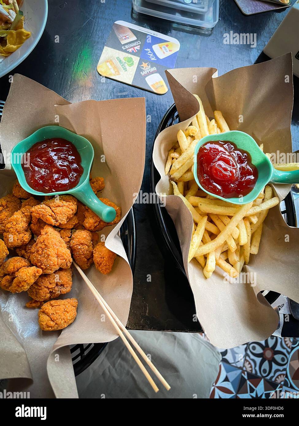 Crispy chicken nuggets bites and French fries served with ketchup in paper-lined baskets on a dark table malaysia snack Stock Photo