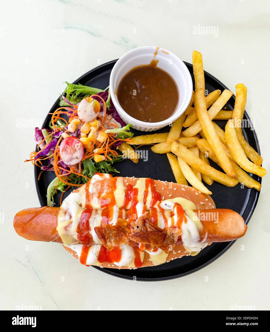 Plate with a hot dog topped with bacon, cheese, and sauces served with fries, salad, and a cup of brown gravy malaysia - Smartphone Captured Stock Image