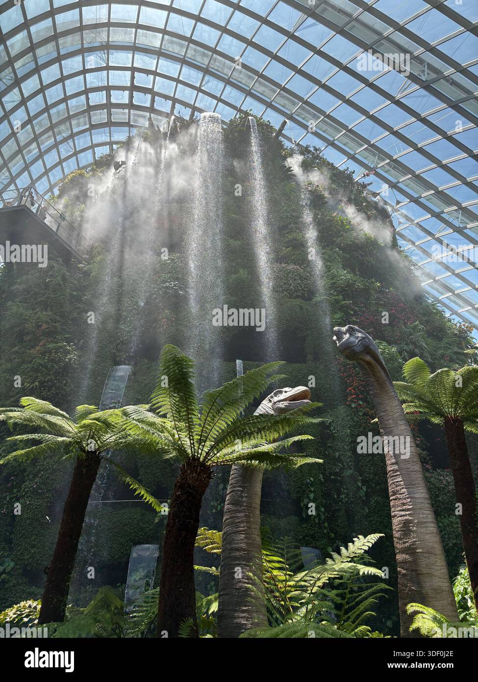 Spectacular indoor botanical garden with a cascading waterfall, tropical plants, and lifelike dinosaur sculptures in Flower Dome, Gardens by the Bay - Smartphone Captured Stock Image