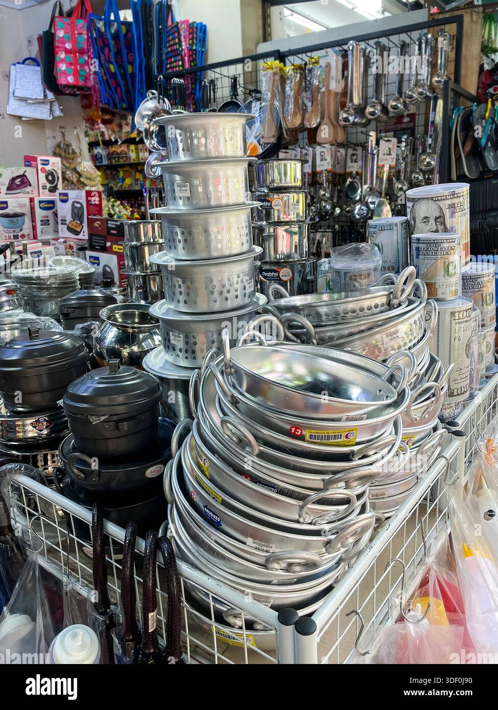 Stacked metal pots, pans, and kitchen utensils displayed for sale in a crowded local hardware or general store in malaysia asia - Smartphone Captured Stock Image