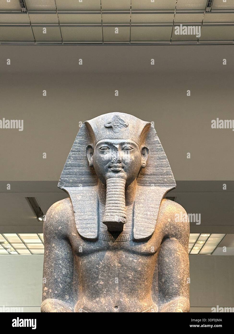 Ancient Egyptian pharaoh statue with nemes headdress and cobra, seated in a museum setting under soft lighting - Smartphone Captured Stock Image
