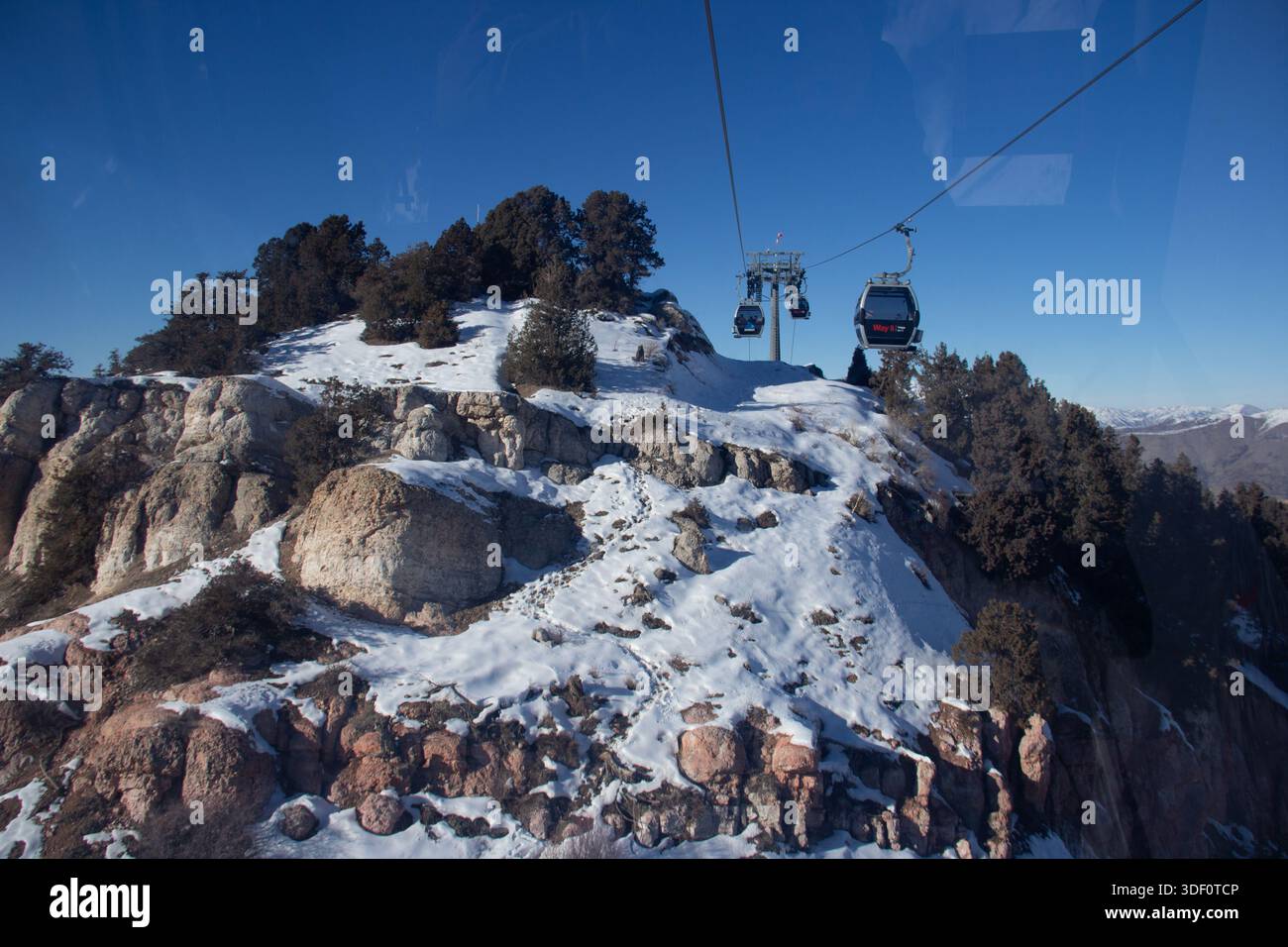 Cable car over snowy mountain rocks and forest in winter. Ski resort infrastructure and mountain transport. Stock Photo