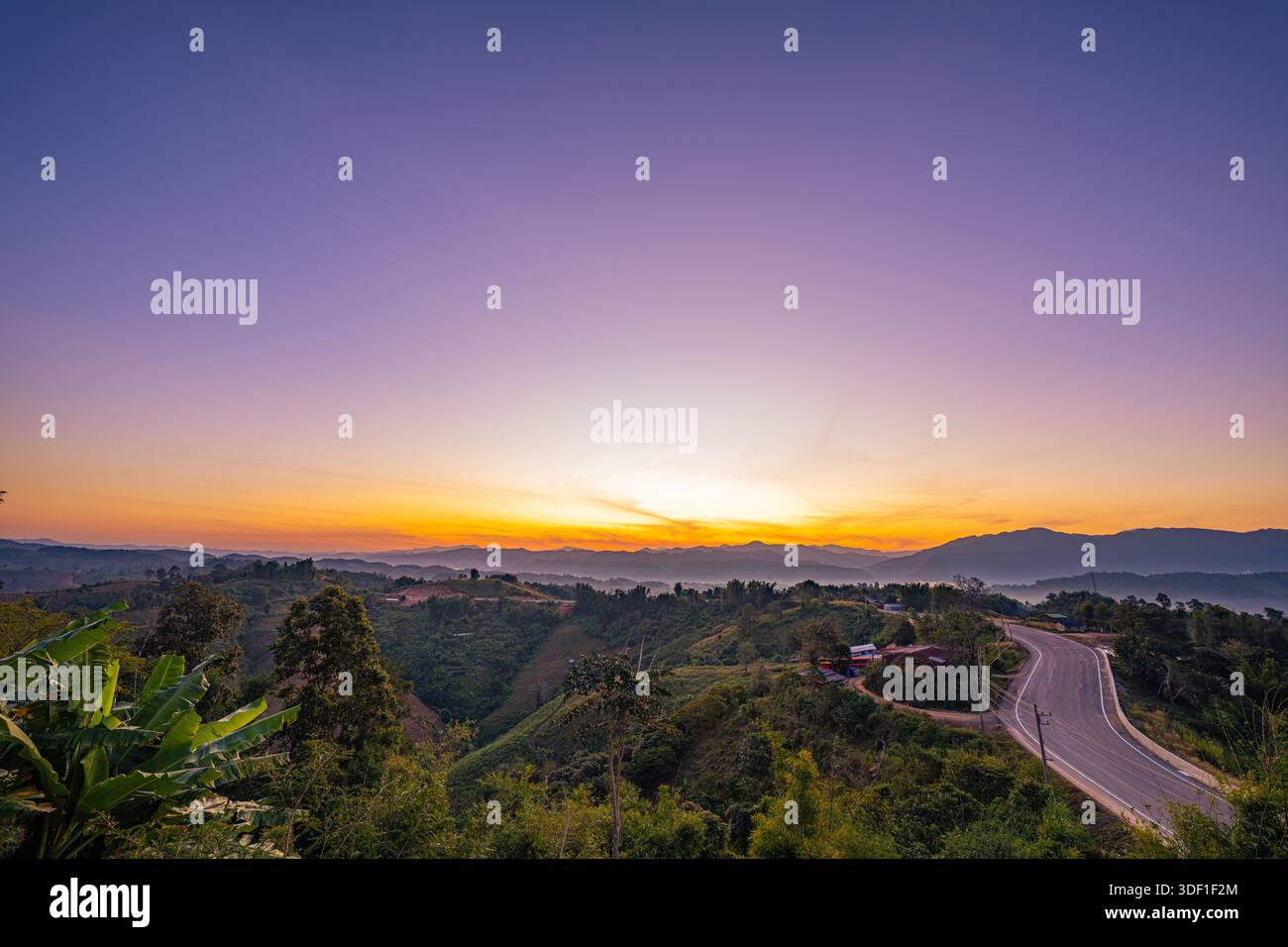 A scenic winding road stretches through lush green hills and layered ...