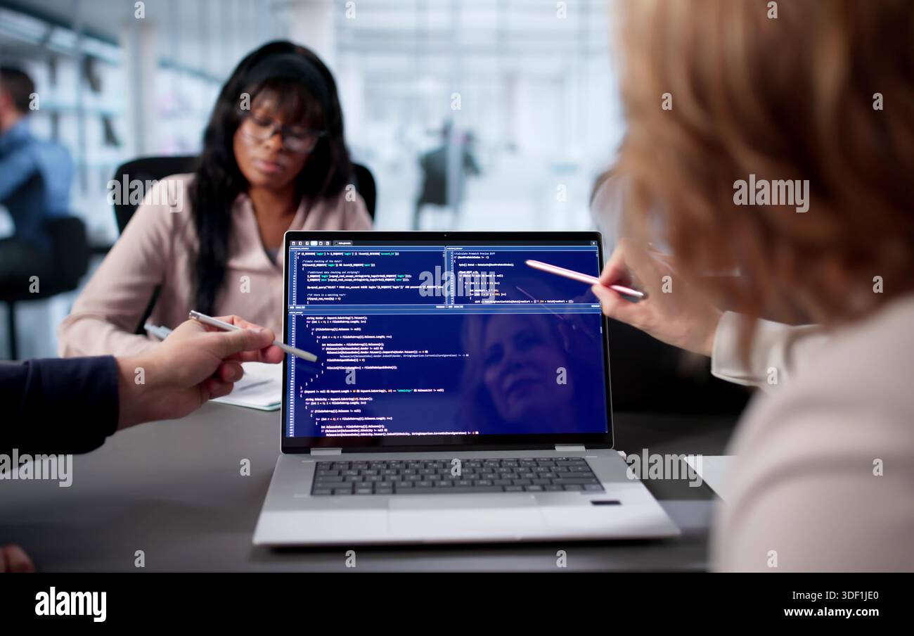 Team Of Engineers Developing Software In Busy Office Environment. Two Programmers Coding Together On Laptop Stock Photo