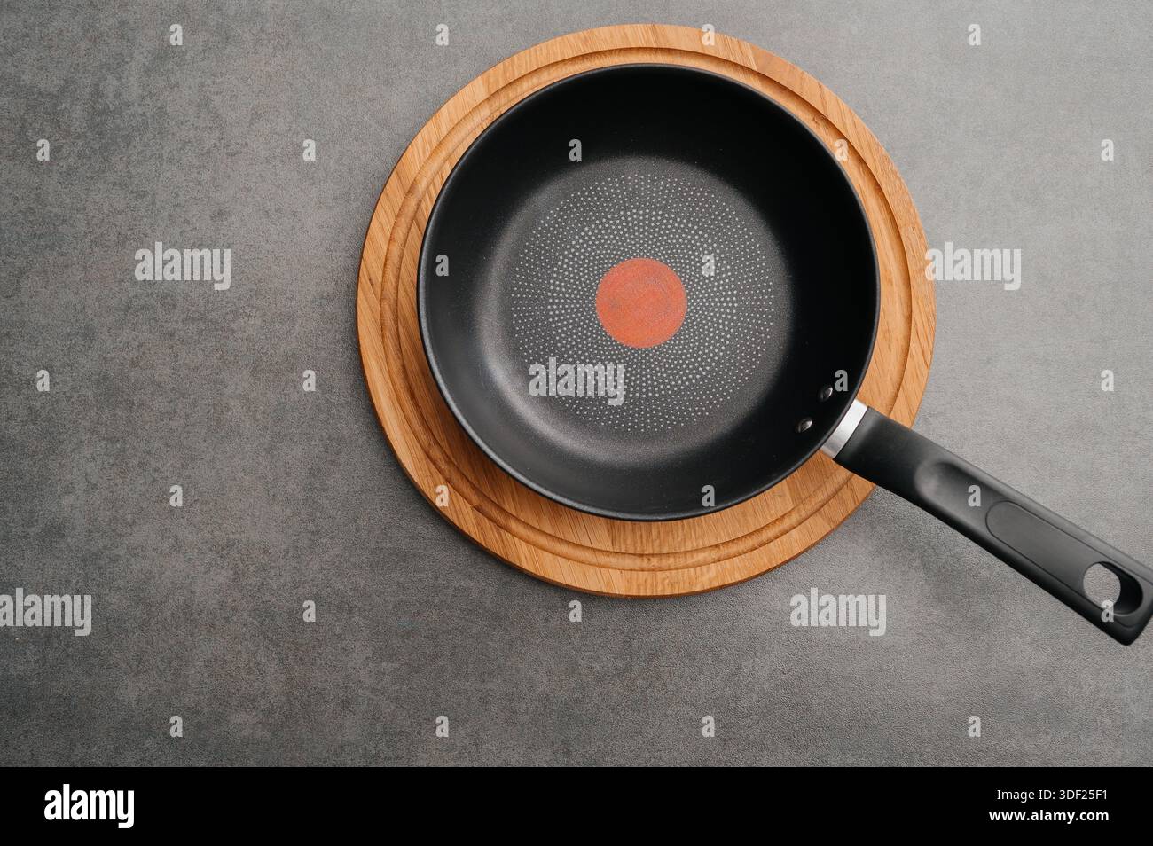 Minimalist presentation featuring skillet on textured surface with heat indicator, Stylish arrangement of nonstick pan on cork mat against textured Stock Photo