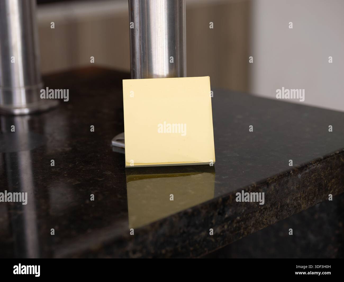 Yellow sticky note on a granite countertop near a metal stand, representing kitchen reminders and home planning. Stock Photo